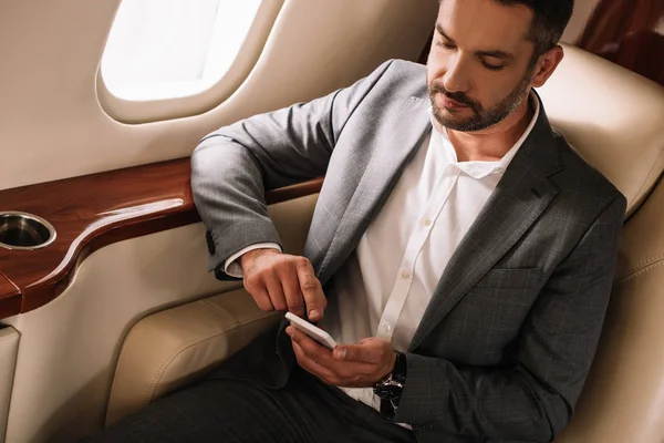 Красивий бородатий бізнесмен використовує смартфон у приватному літаку — стокове фото