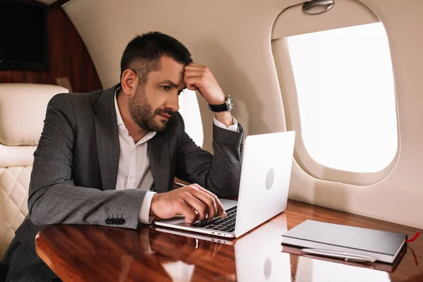 Hombre de negocios barbudo utilizando el ordenador portátil en jet privado - foto de stock