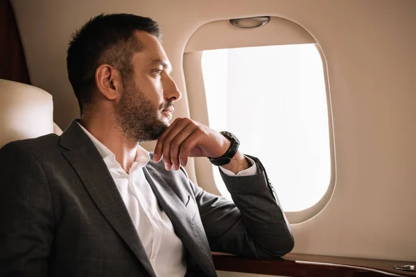 Pensativo hombre de negocios mirando a la ventana del avión - foto de stock