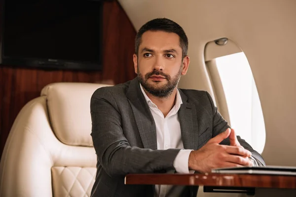 Selective focus of handsome businessman sitting with clenched hands in private jet — Stock Photo