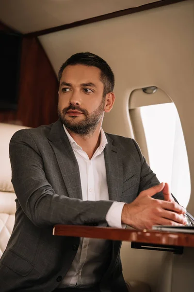 Selective focus of bearded businessman sitting with clenched hands in private jet — Stock Photo