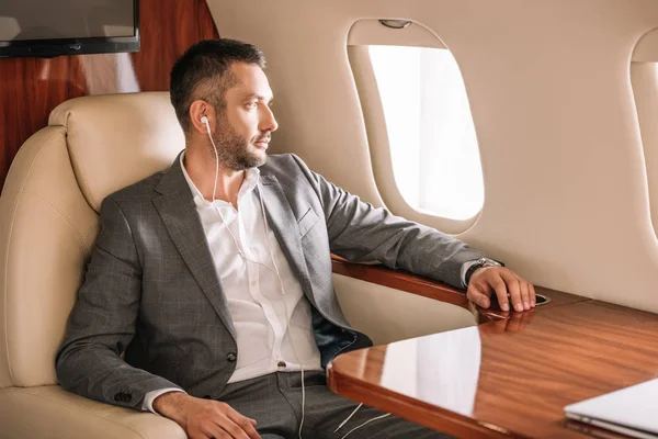 Foyer sélectif de beau homme d'affaires écoutant de la musique et regardant la fenêtre de l'avion — Photo de stock