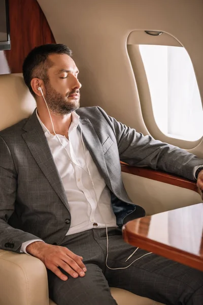 Enfoque selectivo de hombre de negocios guapo con los ojos cerrados escuchando música cerca de la ventana del avión - foto de stock