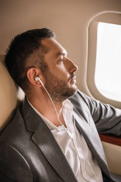 Schöner Geschäftsmann hört Musik in der Nähe des Flugzeugfensters — Stockfoto