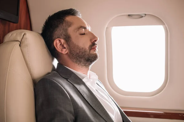 Vue latérale de l'homme d'affaires barbu avec les yeux fermés assis en jet privé — Photo de stock