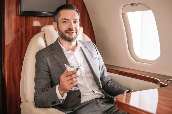 Selective focus of happy businessman holding martini glass with drink in private jet — Stock Photo