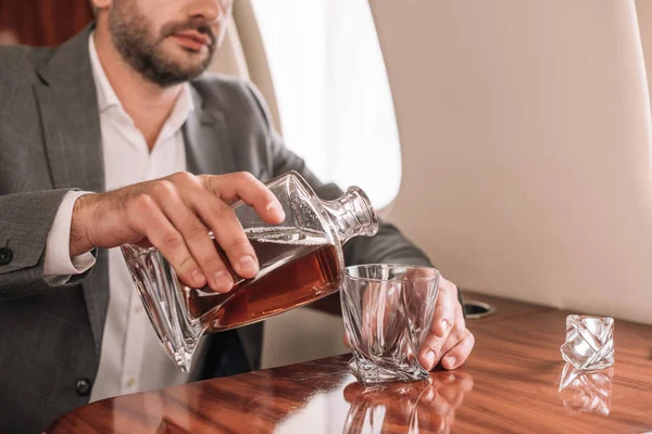 Vue recadrée d'un homme d'affaires barbu versant du whisky dans un verre dans un avion — Photo de stock