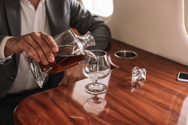 Vista ritagliata di uomo d'affari versando cognac in vetro in jet privato — Foto stock