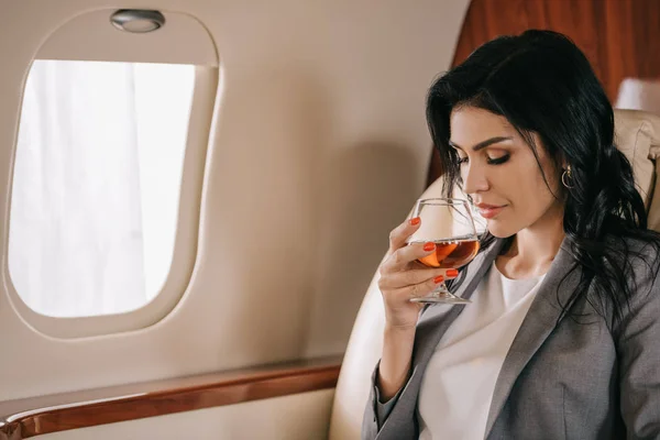 Attraktive Geschäftsfrau hält Glas mit Cognac im Privatjet — Stockfoto
