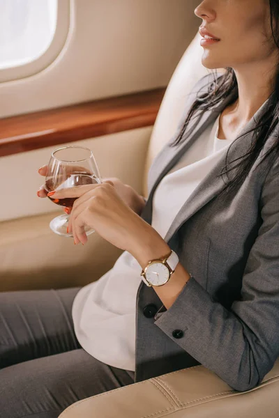 Cropped view of businesswoman in formal wear holding glass with cognac in private jet — Stock Photo