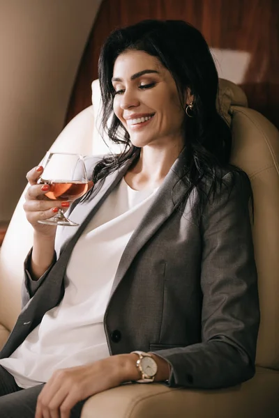 Glückliche Geschäftsfrau in formeller Kleidung mit Glas und Cognac im Privatjet — Stockfoto
