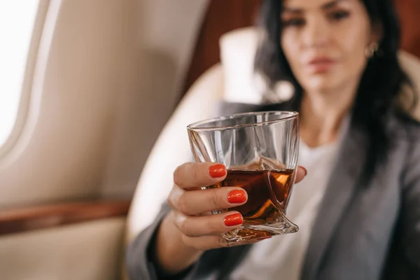 Selective focus of glass with whiskey in hand of businesswoman in private jet — Stock Photo