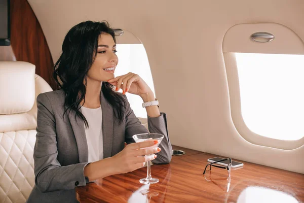 Glückliche Geschäftsfrau in formeller Kleidung hält Martini-Glas mit Alkohol im Privatjet — Stockfoto