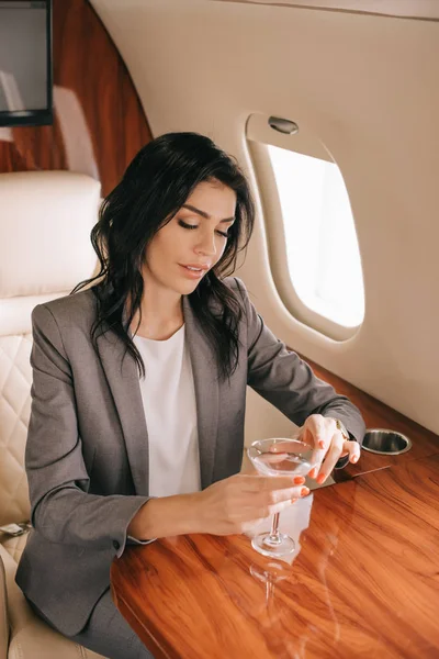 Hermosa mujer de negocios sosteniendo vaso de martini en jet privado - foto de stock