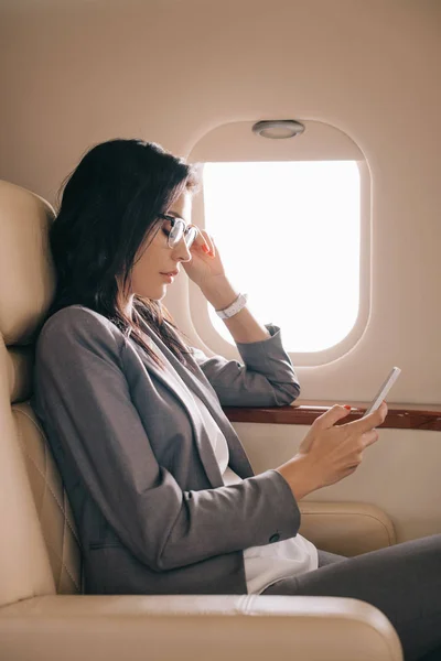 Vista lateral de mujer de negocios en gafas usando smartphone en avión privado - foto de stock