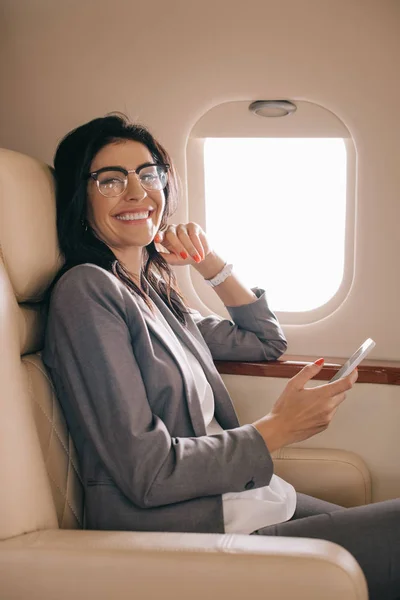 Happy businesswoman in glasses using smartphone in private jet — Stock Photo