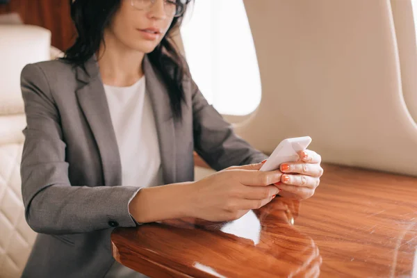 Cropped view of businesswoman holding smartphone in private jet — Stock Photo