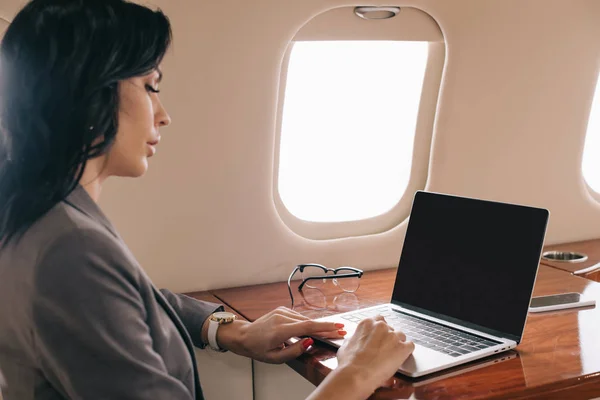 Selective focus of attractive businesswoman using laptop with blank screen in private jet — Stock Photo