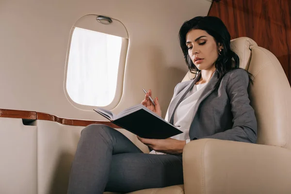 Attractive businesswoman holding pen while looking at notebook in private jet — Stock Photo
