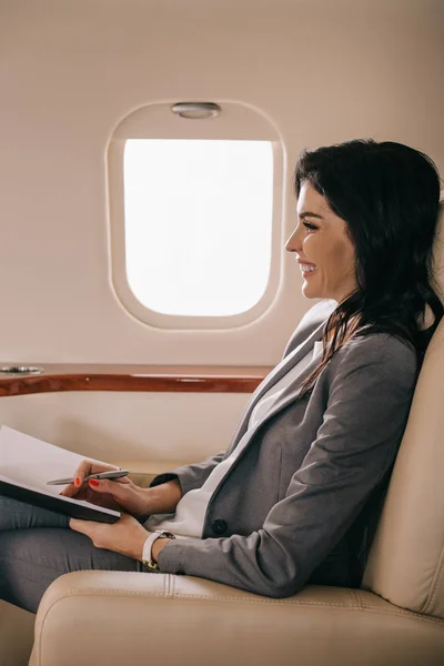 На вид веселої ділової жінки, що тримає ручку і зошит в літаку. — стокове фото