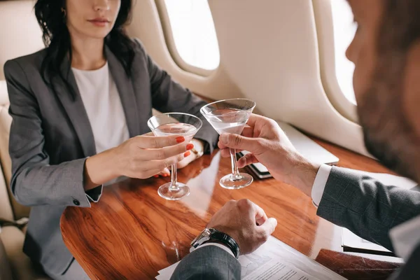 Cropped view of bearded businessman and businesswoman toasting martini glasses in private jet — Stock Photo