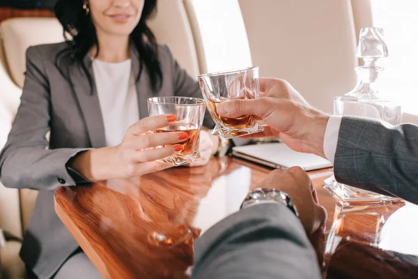 Vista cortada de empresário e empresária brindar copos com álcool em jato particular — Fotografia de Stock
