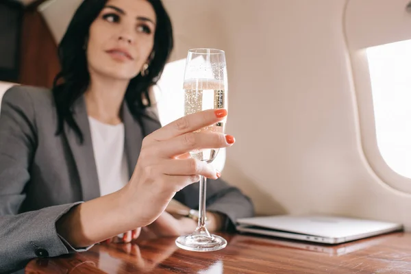 Selective focus of champagne glass in hand of attractive businesswoman in plane — Stock Photo