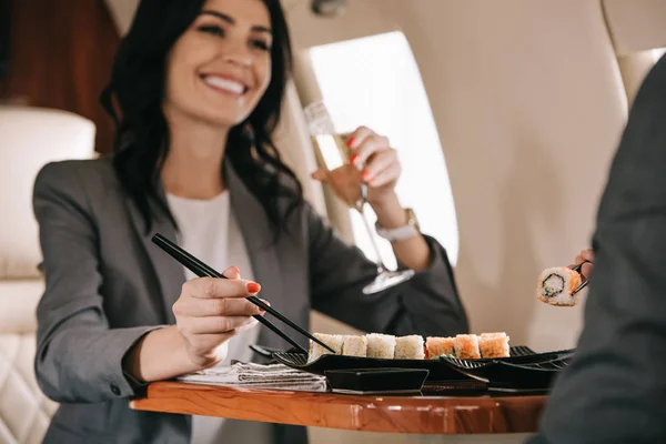 Vista recortada de hombre de negocios cerca de mujer de negocios feliz con copa de champán y sushi sabroso - foto de stock