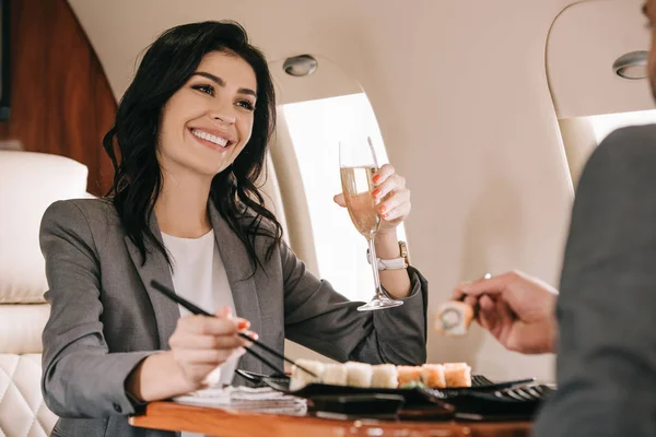 Vista ritagliata di uomo d'affari vicino a donna d'affari allegra con bicchiere di champagne e sushi saporito — Foto stock