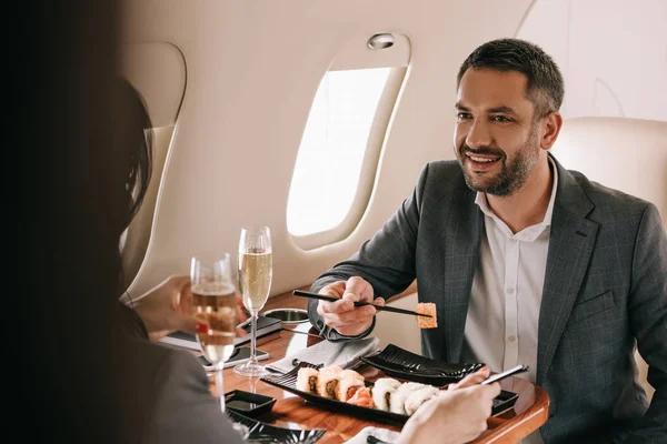 Vue recadrée de femme d'affaires près de l'homme d'affaires joyeux et savoureux sushi en jet privé — Photo de stock