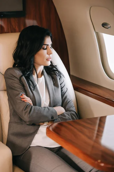 Selective focus of attractive businesswoman with closed eyes and crossed arms sitting in private jet — Stock Photo