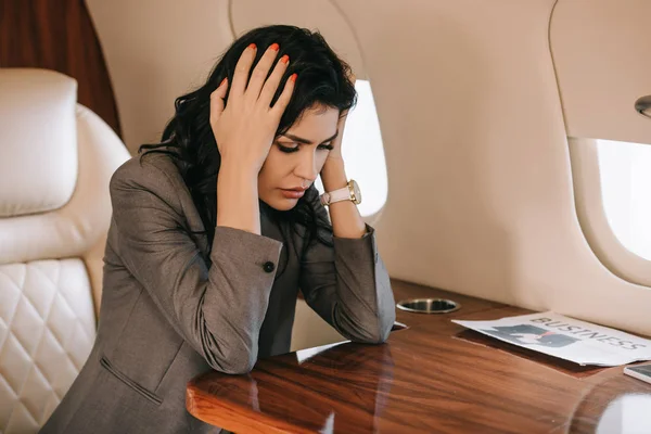 Selective focus of tired businesswoman touching head while sitting in private jet — Stock Photo