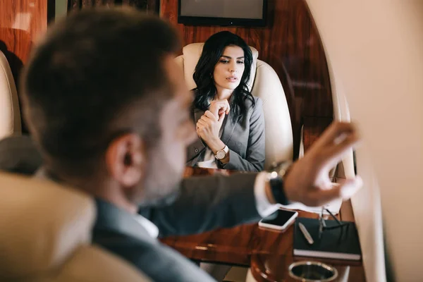 Selective focus of worried businesswoman with fear of flight sitting with businessman in private jet — Stock Photo