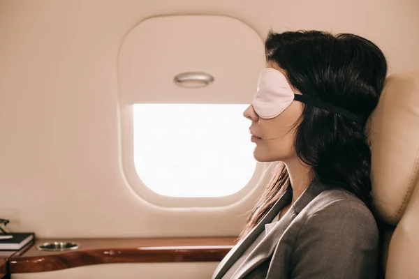 Vista lateral de la mujer de negocios en la máscara de dormir sentado en jet privado - foto de stock