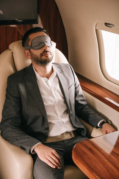Bearded businessman in sleeping mask sitting in private jet — Stock Photo