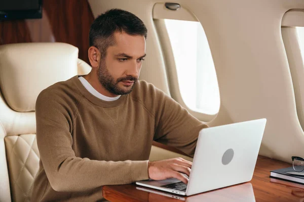 Hombre barbudo guapo usando el ordenador portátil en jet privado - foto de stock