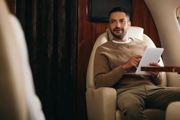 Selective focus of handsome bearded man using digital tablet in private jet — Stock Photo