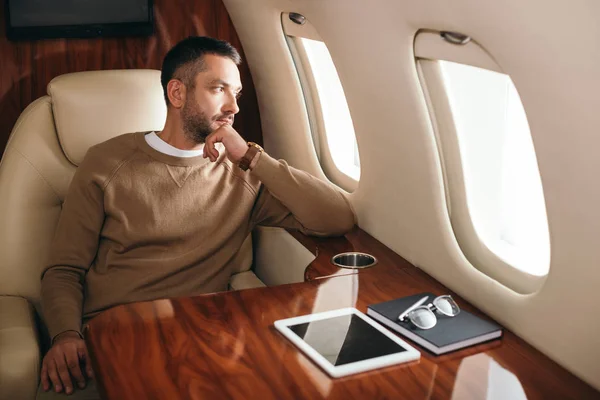 Bel homme barbu regardant la fenêtre de l'avion dans la première classe de jet privé — Photo de stock