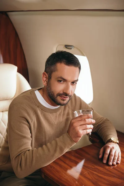 Handsome bearded man holding glass with alcohol drink while sitting in first class of private jet — Stock Photo