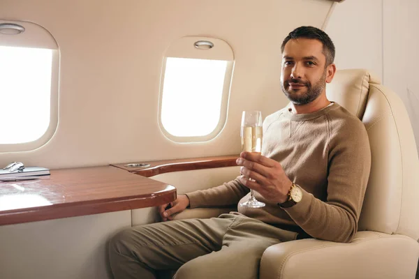 Hombre alegre sosteniendo copa de champán mientras está sentado en primera clase de jet privado - foto de stock