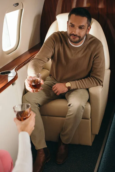 Cropped view of woman clinking glasses with handsome man in private jet — Stock Photo