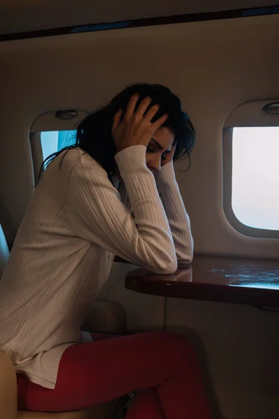 Испуганная женщина с воздушной болезнью трогает волосы в частном самолете — стоковое фото