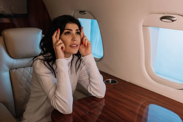 Mujer asustada sentada con los dedos cruzados en jet privado - foto de stock