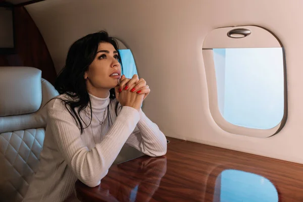 Scared woman sitting with praying hands in private jet — Stock Photo