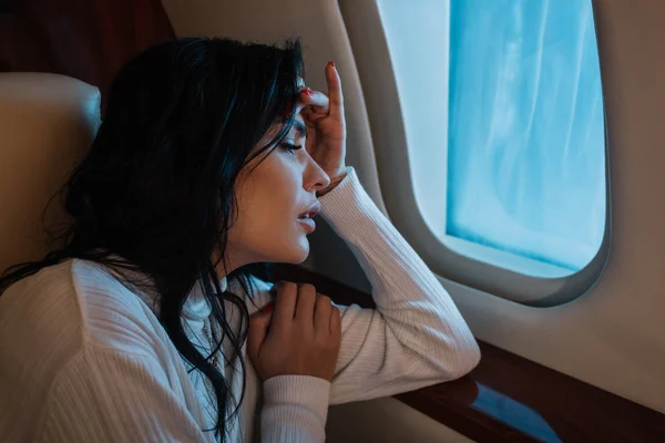 Scared woman with airsickness looking at airplane window in private jet — Stock Photo