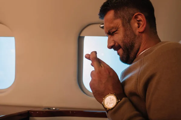 Scared man with closed eyes and fingers crossed in private jet — Stock Photo