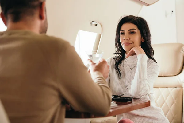 Selective focus of attractive woman clinking martini glasses with bearded man in private jet — Stock Photo