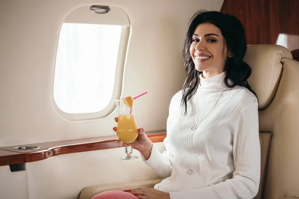 Cheerful woman holding tasty cocktail in private jet — Stock Photo