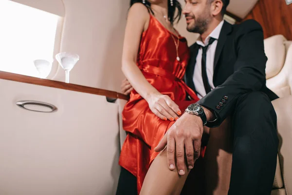 Ausgeschnittene Ansicht eines bärtigen Mannes, der eine Frau im roten Kleid in der ersten Klasse eines Privatjets berührt — Stockfoto
