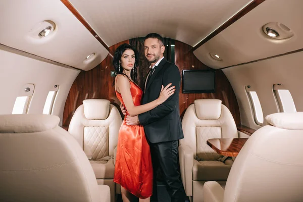 Attrayant femme en robe rouge debout avec bel homme barbu en jet privé — Photo de stock